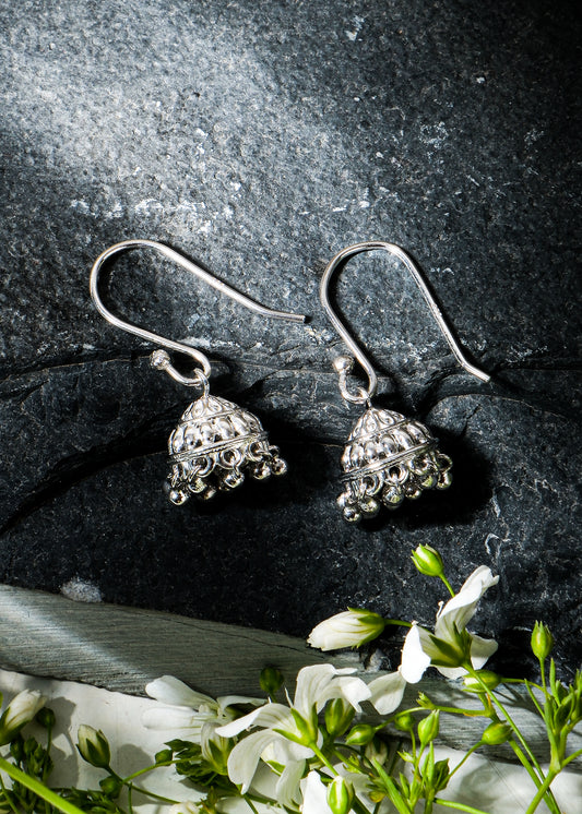 Silver earrings on a dark stone surface with greenery